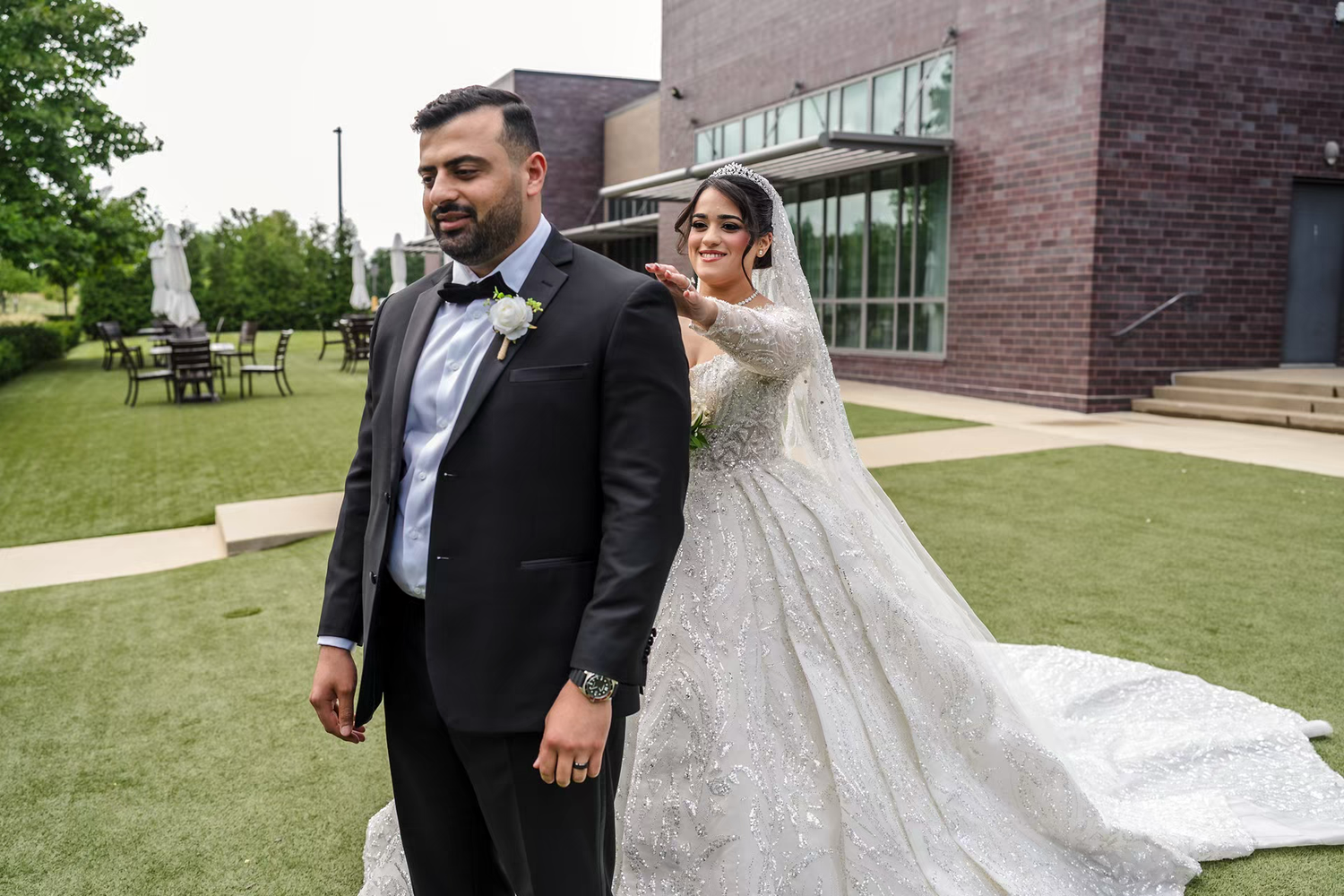 Bride in elegant ball gown and groom in black first look at renaissance outdoor wedding venue.