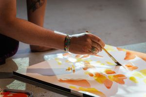 Artist painting colorful watercolor flowers on canvas with a brush, wearing bracelets and a ring.