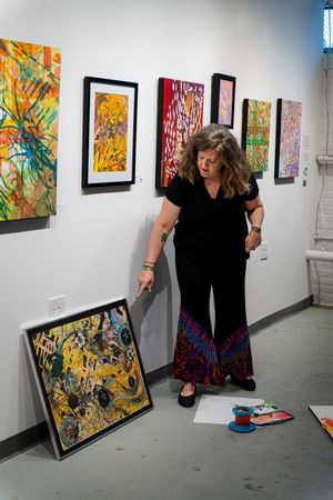 Woman in black outfit examines colorful abstract paintings leaning against wall in art gallery exhibition.