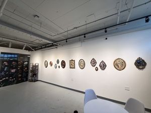 Art gallery wall displaying decorative ceramic plates and mixed media wall art pieces in a modern white exhibition space.
