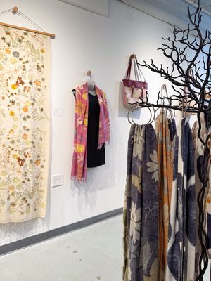 Boutique display featuring floral textiles, a pink scarf on mannequin, patterned bag, and garments on a decorative branch rack.