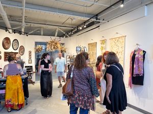 Visitors explore colorful textile art and mixed media pieces displayed on walls inside a bright contemporary art gallery.