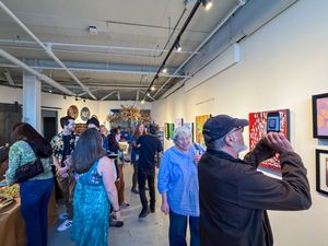 Art gallery opening reception with guests mingling among vibrant paintings on white walls.