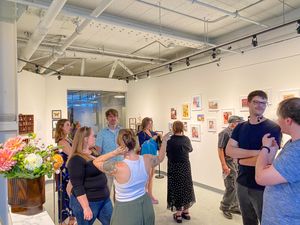 People mingling at an art gallery opening with colorful artwork displayed on white walls and fresh flowers in foreground.