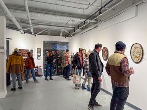 Visitors browse artwork at a contemporary art gallery opening, with white walls and industrial ceiling.