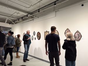 People viewing ornate framed artwork on white gallery walls during an art exhibition opening.