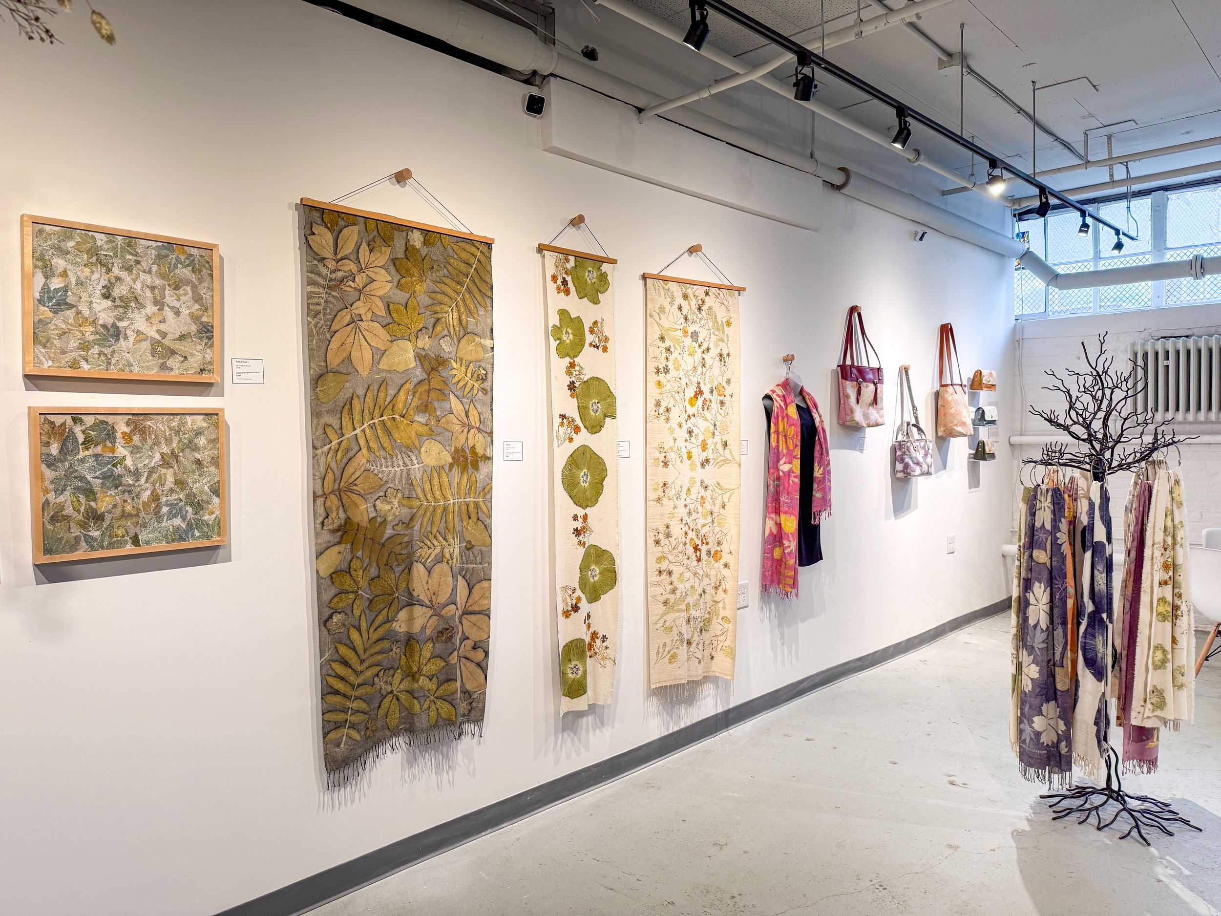 Art gallery wall displaying botanical textile hangings and framed prints with floral motifs in earthy greens and neutrals.