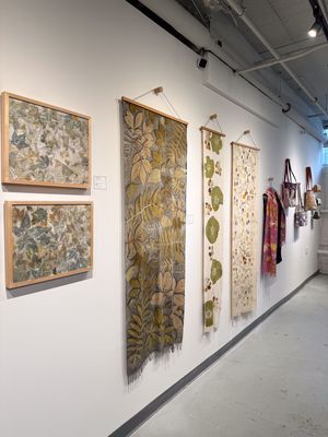 Gallery wall displaying botanical leaf print textiles and framed artwork in muted green and earth tones.