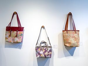 Three floral fabric handbags with leather trim displayed on a white gallery wall, including tote and crossbody styles.