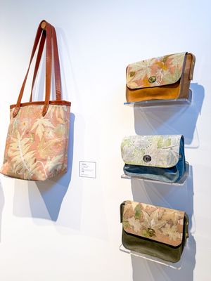 Four floral fabric handbags displayed on a white gallery wall, including a tote bag with leather straps and three clutch purses.