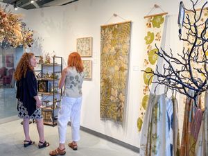 Two women admire botanical textile wall art and decor in a bright gallery shop filled with nature-inspired artwork.