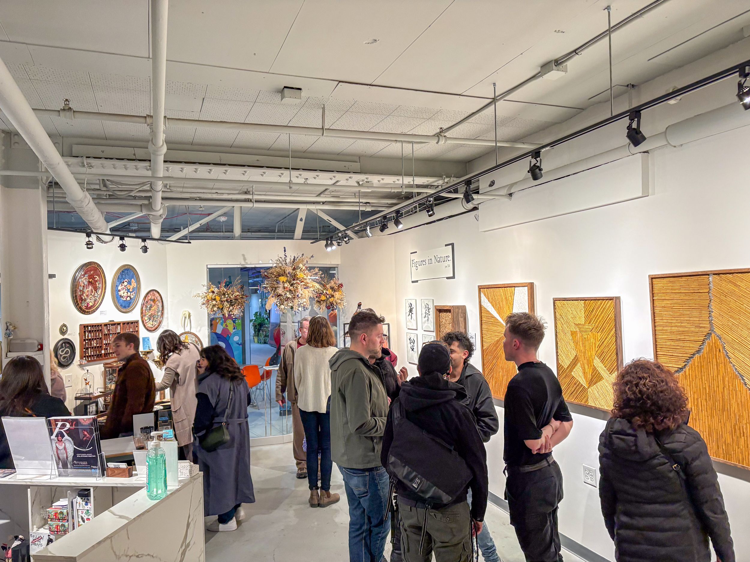 Visitors browsing colorful artwork and paintings displayed on white walls inside a modern art gallery.