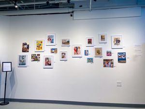 Art gallery wall displaying a colorful collection of framed prints and illustrations arranged in a modern white exhibition space.