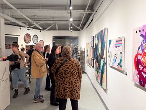 Visitors browse colorful modern artwork displayed on white gallery walls during an art show opening reception.