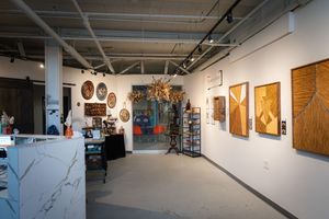 Modern art gallery interior featuring wooden wall art, decorative plates, and a marble reception desk.