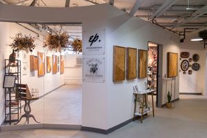 Modern art gallery showroom featuring wooden wall art, hanging botanical sculptures, and eclectic decor displays in a bright white space.