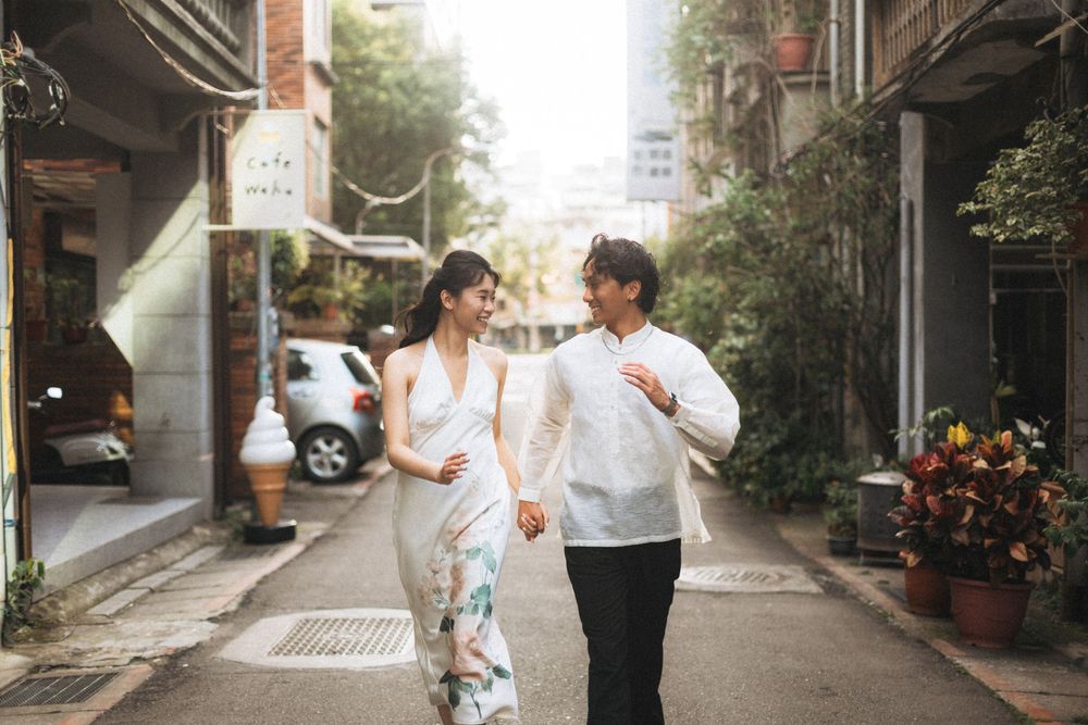 Couple holding hands and walking through a charming urban alley with lush greenery and vintage storefronts.