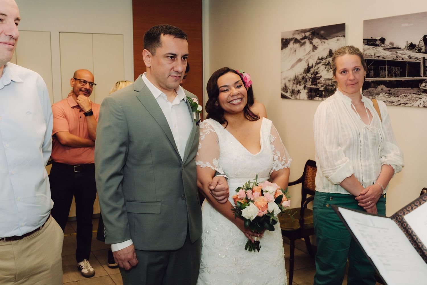 Bride and groom stand together during civil wedding ceremony with guests watching in background.