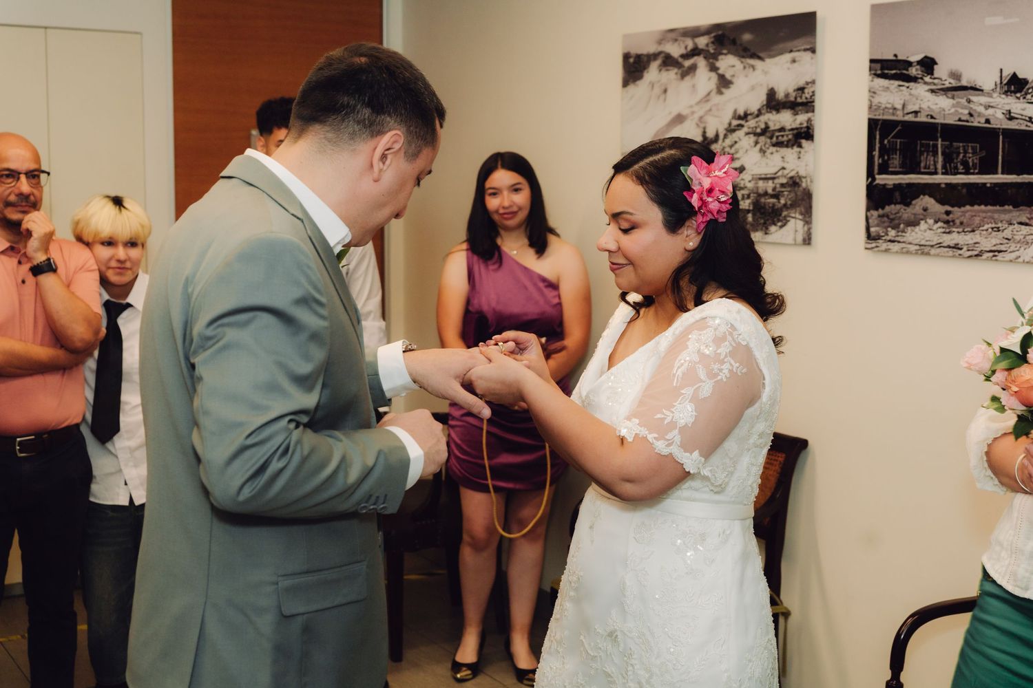 Couple exchanges wedding rings during civil ceremony while officiant holds bridal bouquet.