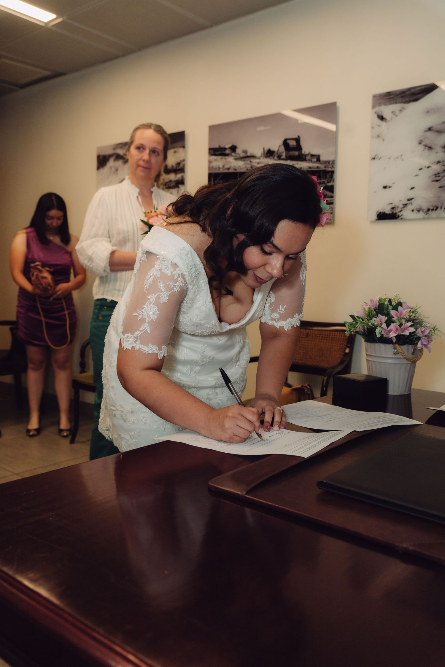Bride signs official wedding documents at wooden desk during civil marriage ceremony.