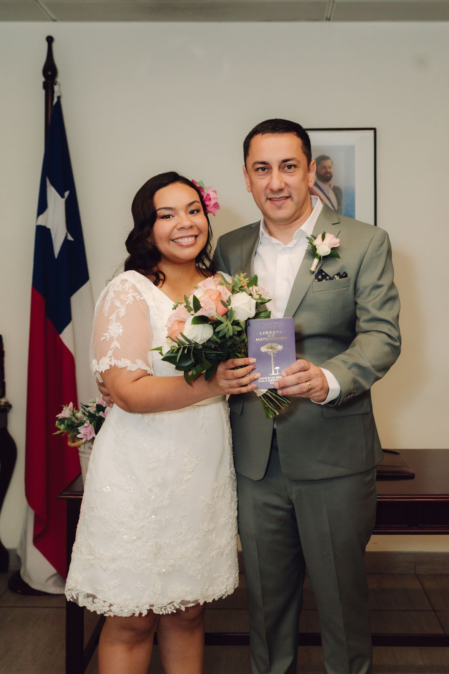 Happy couple poses with wedding bouquet and marriage certificate before Texas flag at civil ceremony.