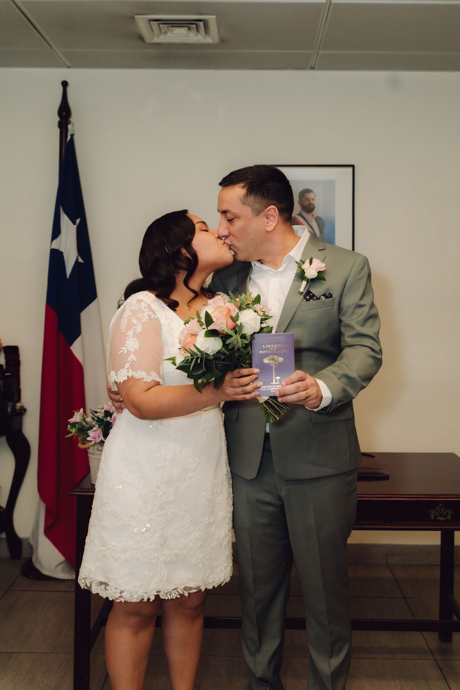Newlyweds share first kiss holding pink bouquet and marriage book at Texas courthouse wedding ceremony.