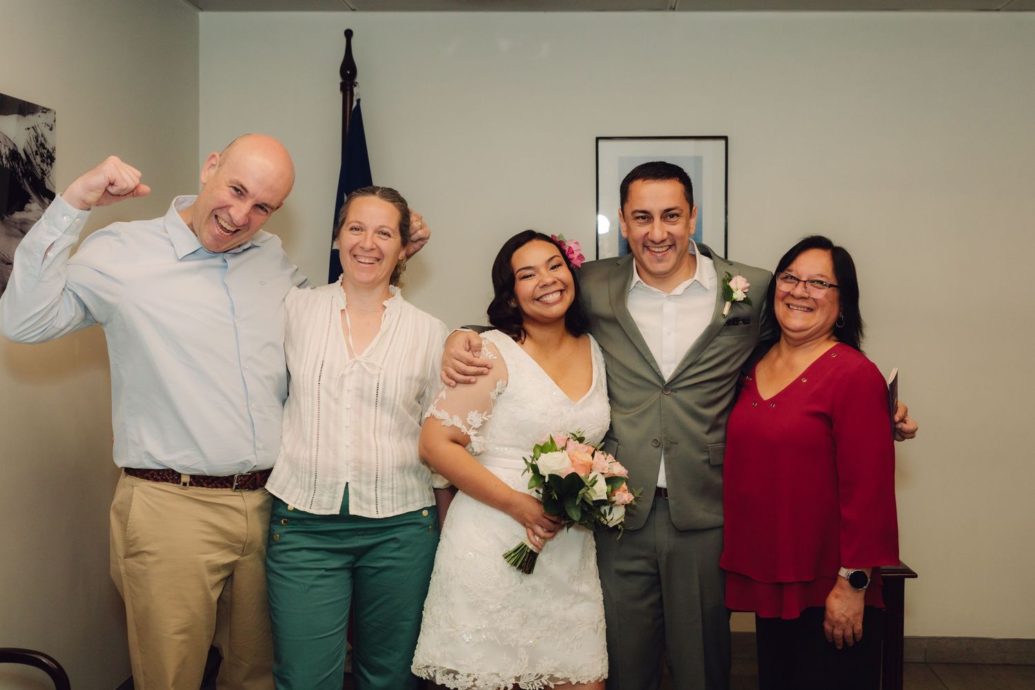 Joyful wedding guests celebrate with bride and groom in white lace dress at intimate courthouse ceremony.