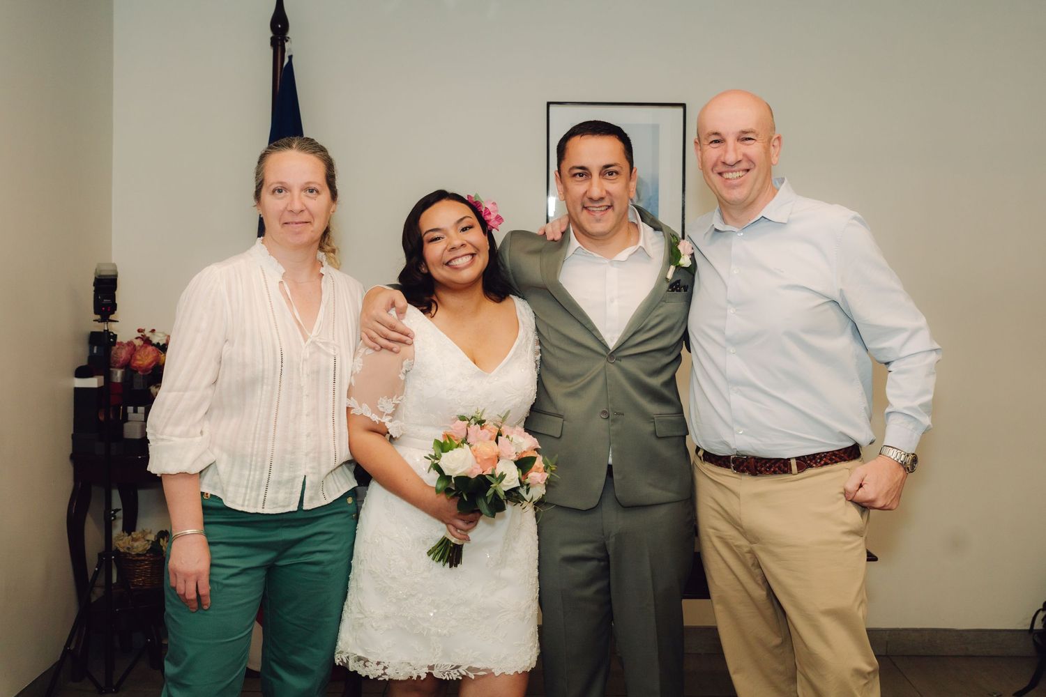 Bride holding pink bouquet poses with groom in gray suit and two guests at courthouse wedding.