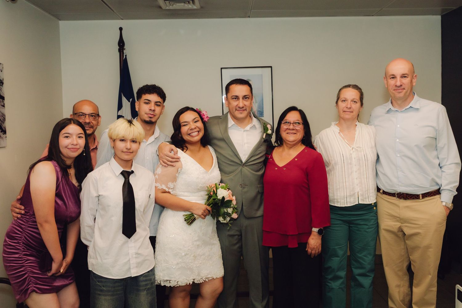 Large wedding party group portrait with bride in white lace and groom in gray suit at courthouse.