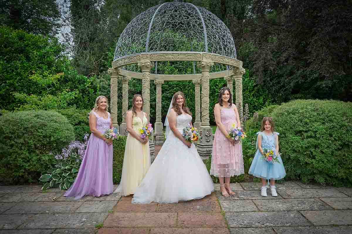Bride and bridesmaids pose in front of the gazebo at Dalston Hall