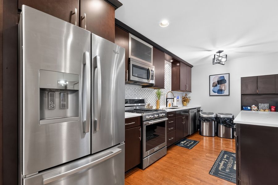Modern kitchen with stainless steel appliances, dark wood cabinets, hardwood floors, and decorative backsplash tile.
