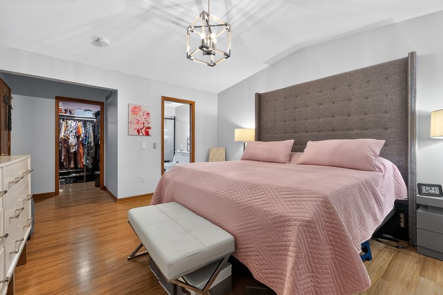 Spacious master bedroom with tufted headboard, pink bedding, chandelier, and walk-in closet on hardwood floors.