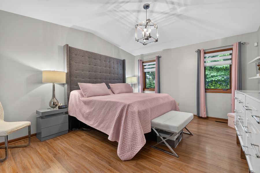 Spacious bedroom with king bed, pink bedding, hardwood floors, chandelier, and large windows with pink curtains.