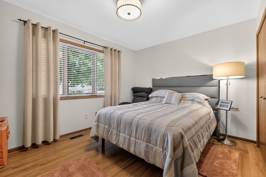 Cozy bedroom with queen bed, striped bedding, hardwood floors, and natural light from window.