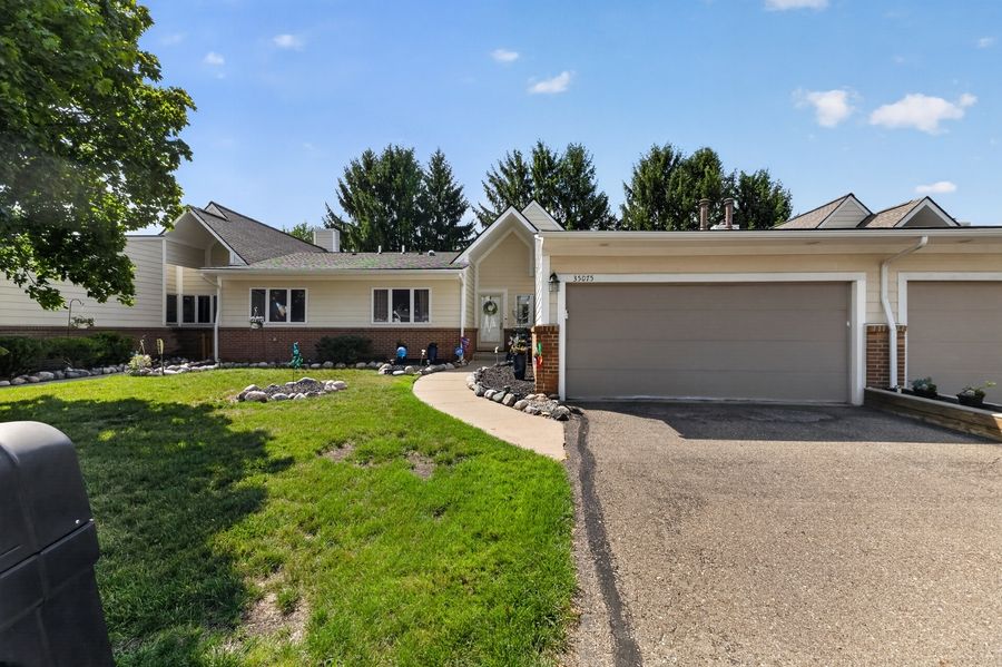 Ranch-style home with brick facade, two-car garage, manicured lawn, and mature trees on a sunny day.