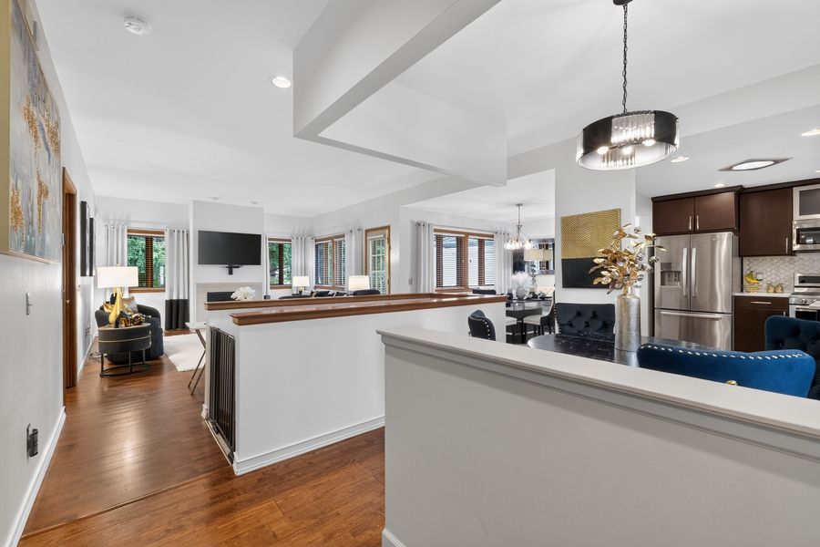 Open-concept kitchen with dark wood floors, pendant lighting, white walls, and stainless steel refrigerator visible in background.
