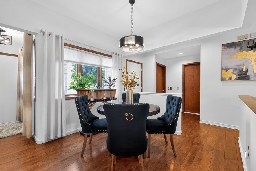 Elegant dining room with round black table, velvet chairs, pendant light, hardwood floors, and bright window with white curtains.