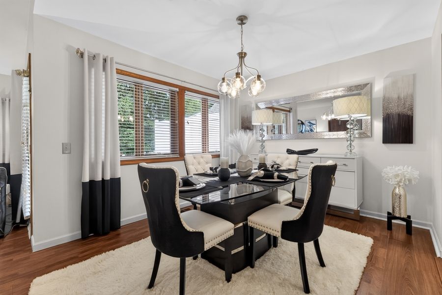 Elegant dining room with black glass table, upholstered chairs, hardwood floors, and chandelier lighting.