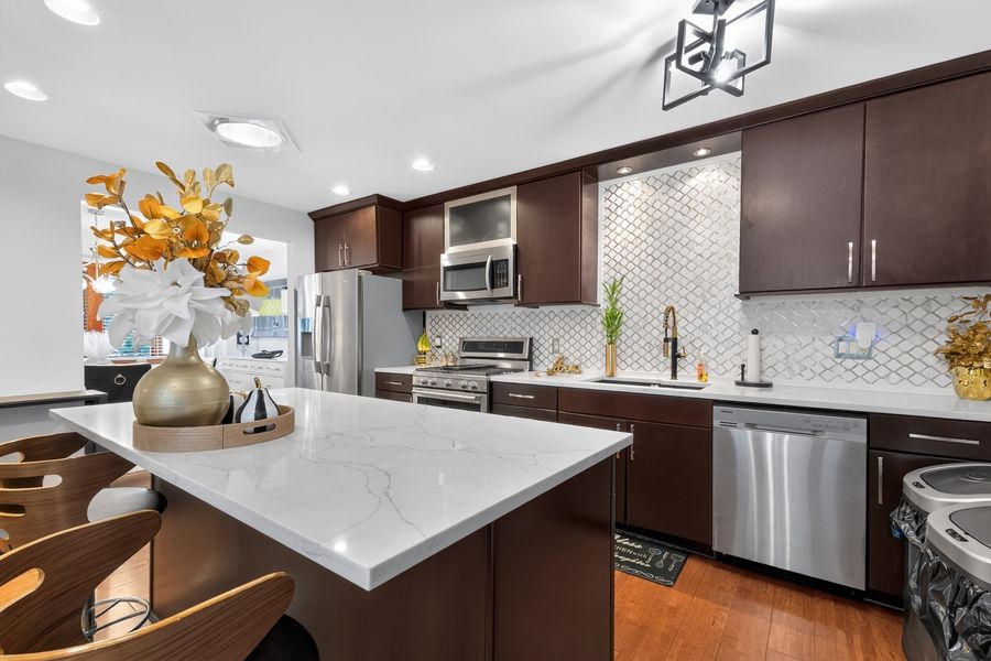 Modern kitchen with dark cabinets, marble island, stainless steel appliances, and white geometric tile backsplash.
