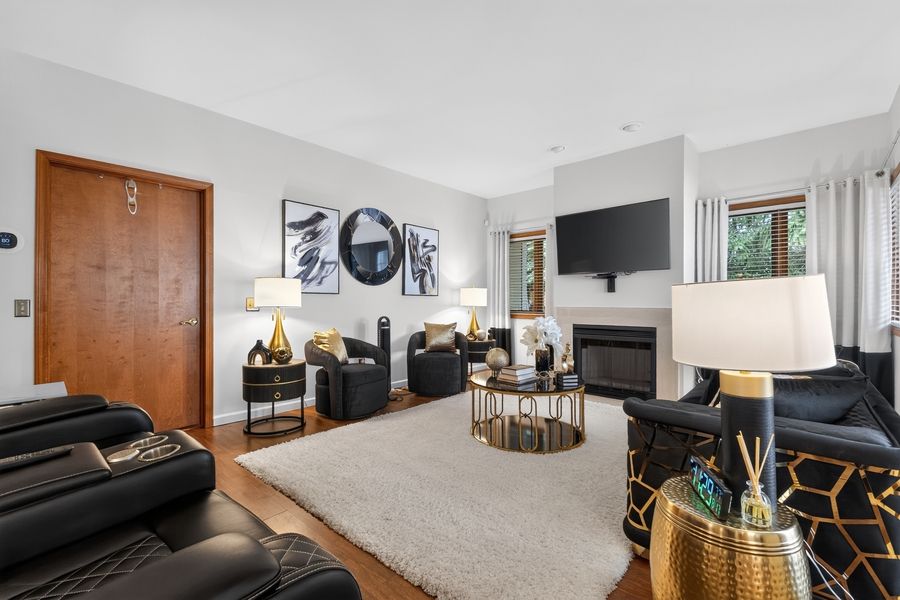 Elegant living room with black leather sofas, white shag rug, gold accents, fireplace, and wall-mounted TV.