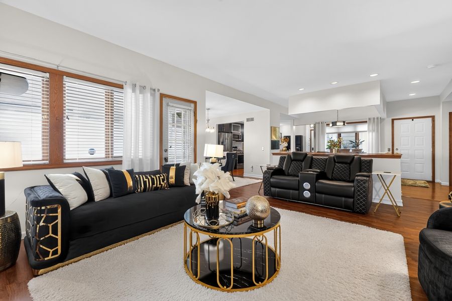 Elegant living room with black and gold sofas, marble coffee table, hardwood floors, and open concept layout.