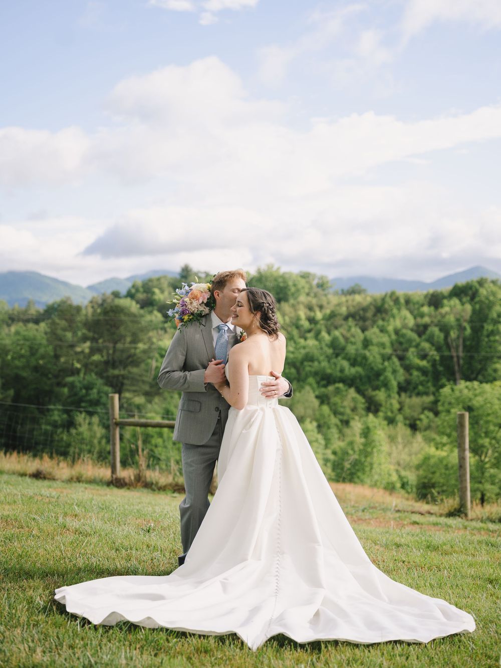 Bride and groom share a romantic moment in a lush green mountain landscape on their wedding day.