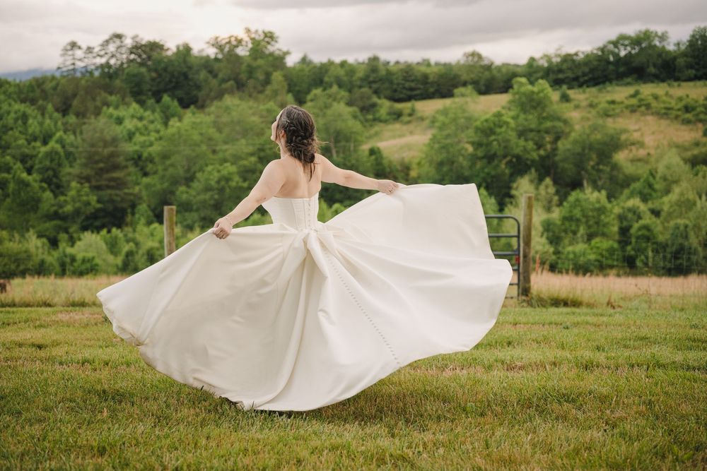 Bride twirling in a flowing white strapless wedding gown in a green countryside field.