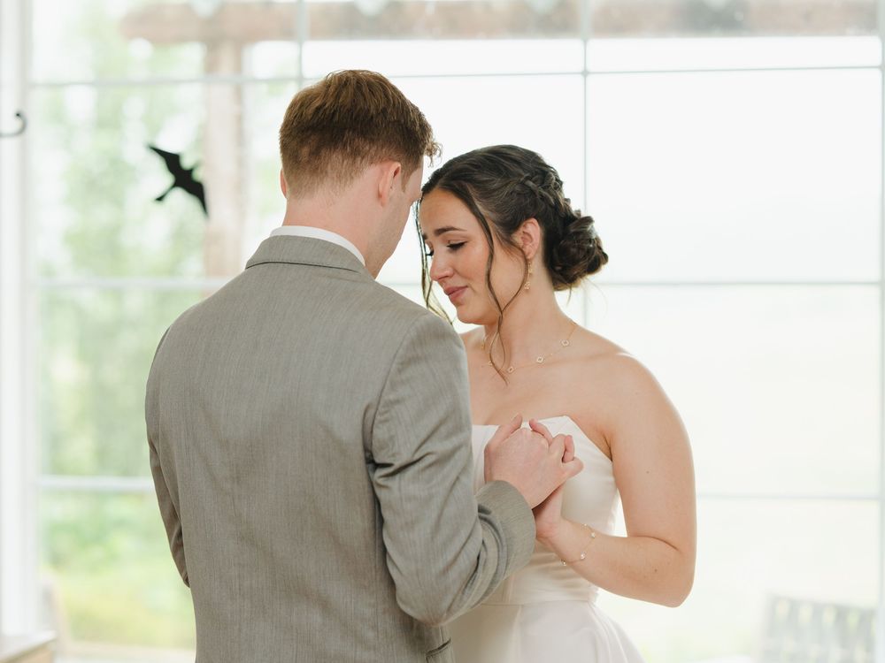 A bride and groom share an intimate first dance moment, she in a strapless gown, he in a light gray suit.
