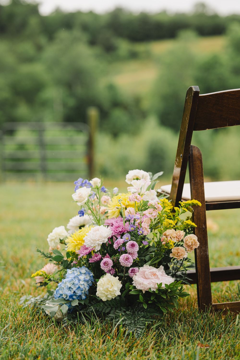 Colorful floral arrangement with pink, white, blue, and yellow blooms beside a wooden folding chair.