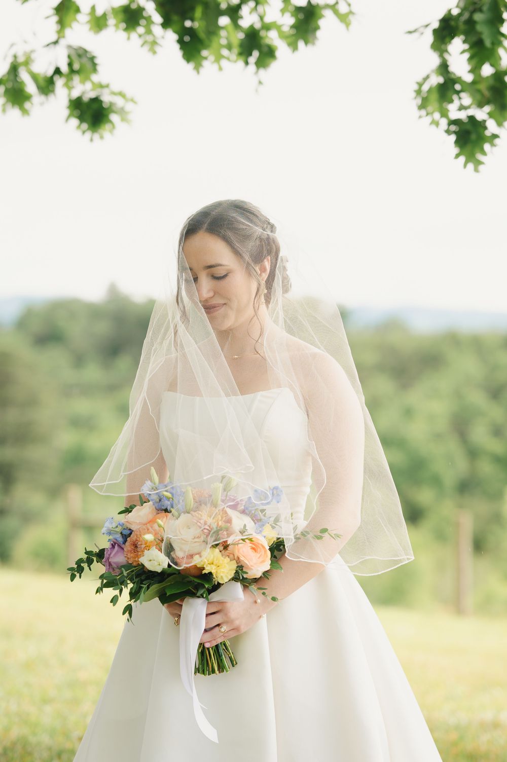 Bride in white gown and veil holding colorful spring bouquet outdoors on wedding day.