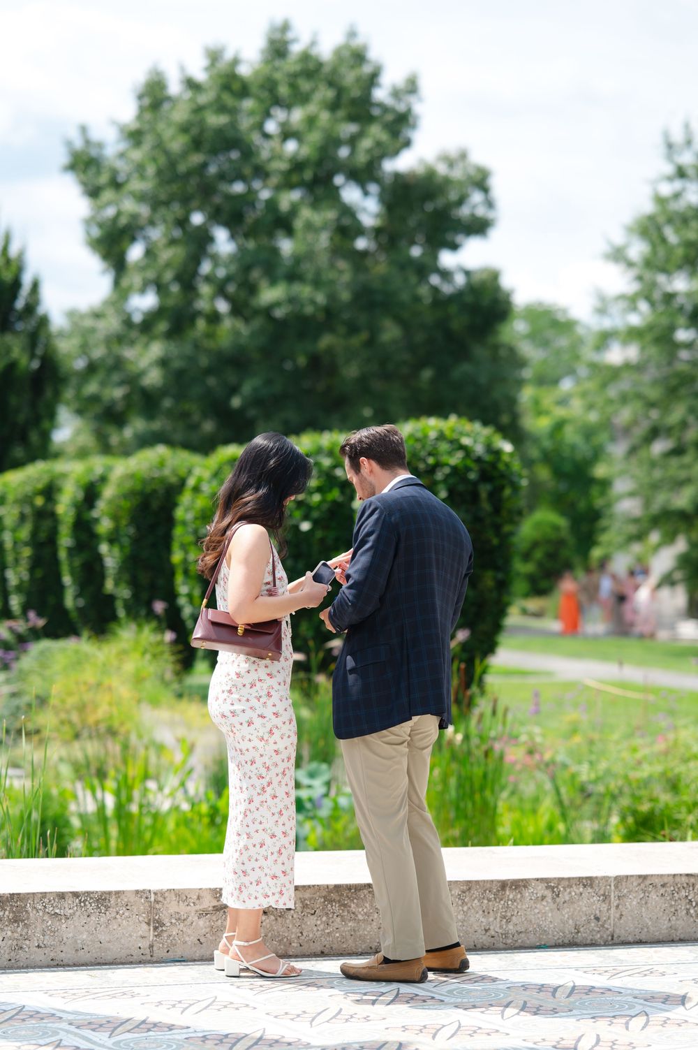 Couple standing together in a lush garden, sharing a tender moment by a stone ledge.
