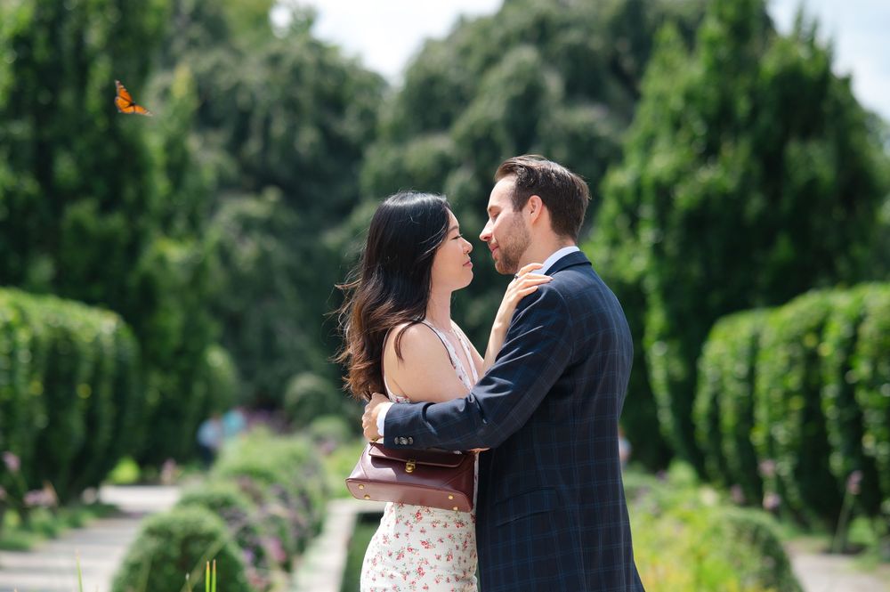 Couple sharing a romantic moment in a lush green garden alley, with a butterfly visible in the background.