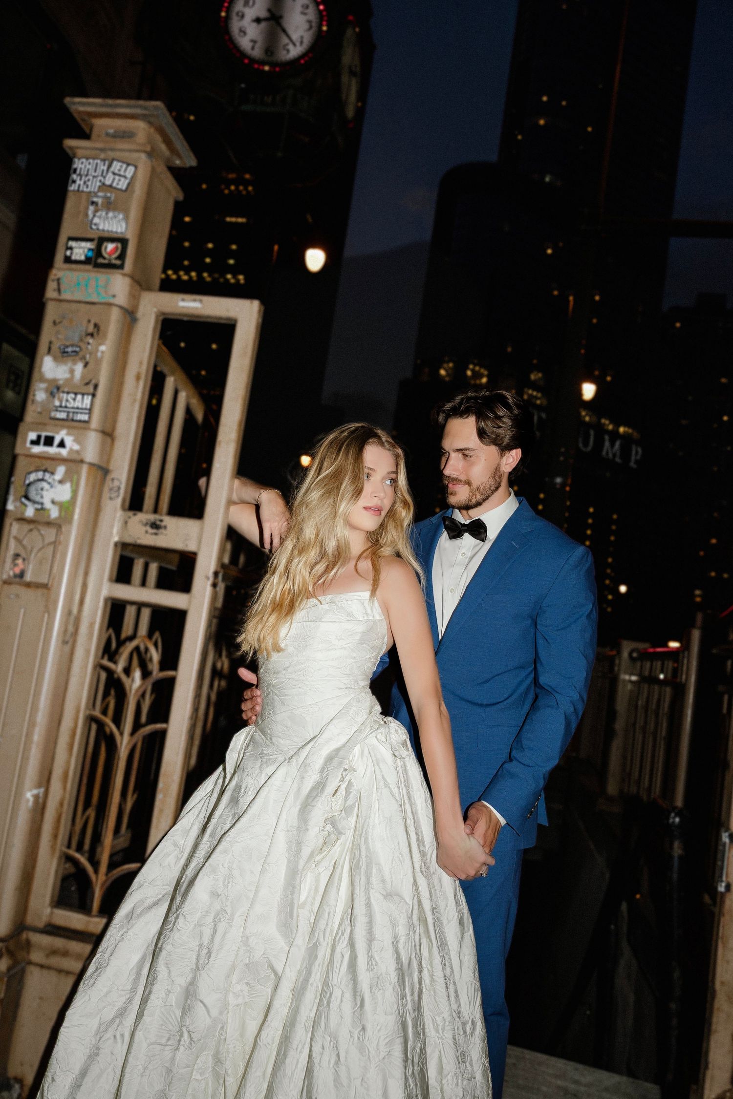 Bride in white ball gown and groom in blue tuxedo hold hands at night in Downtown Chicago.