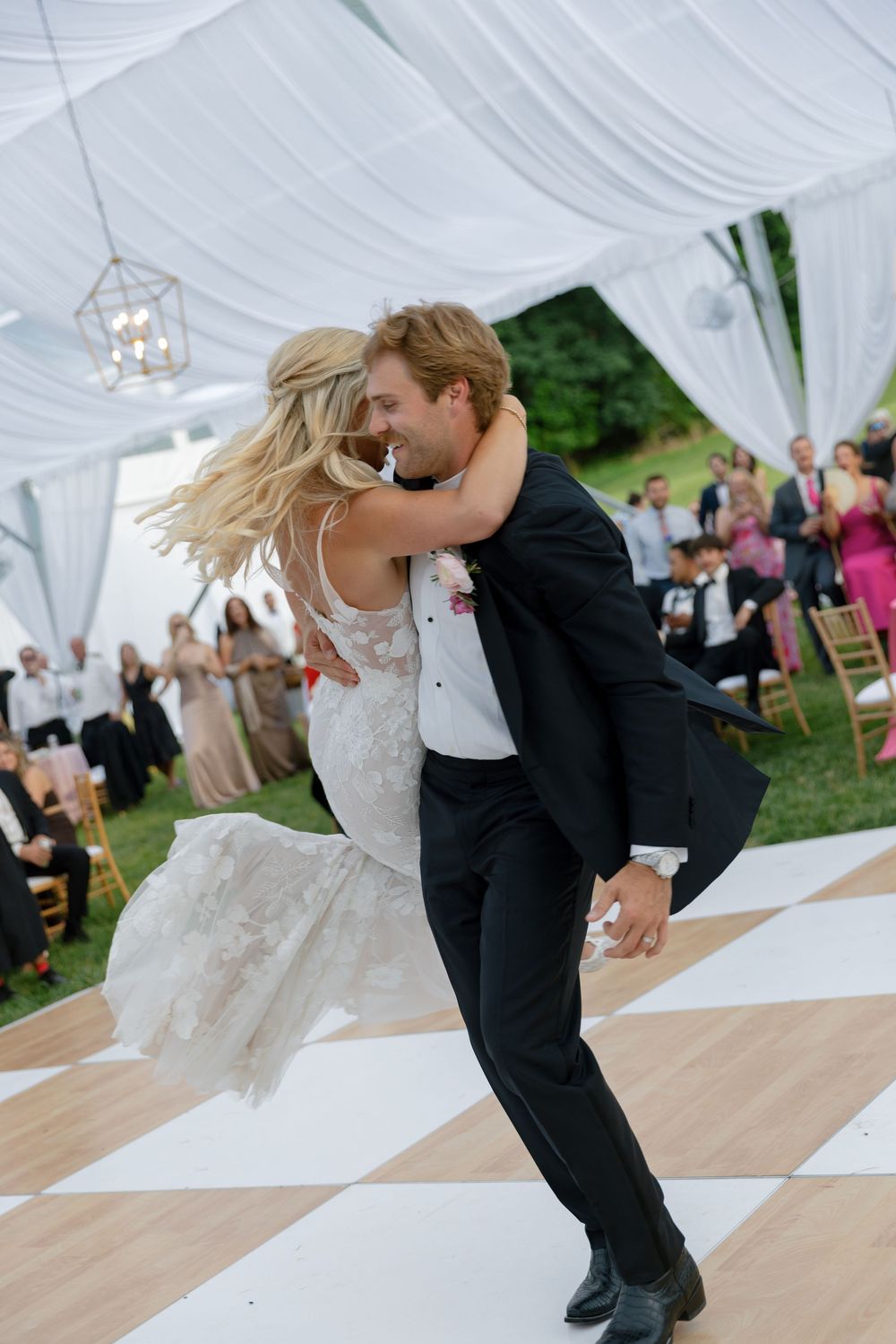 Bride and groom share joyful first dance under elegant draped tent at outdoor wedding reception.